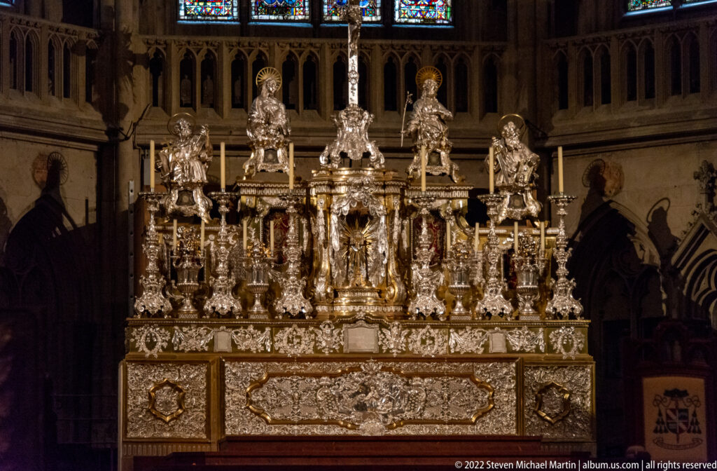 Highly ornate silver altar with standing saints, candles, relief panels, columns, and central sculptural figure.