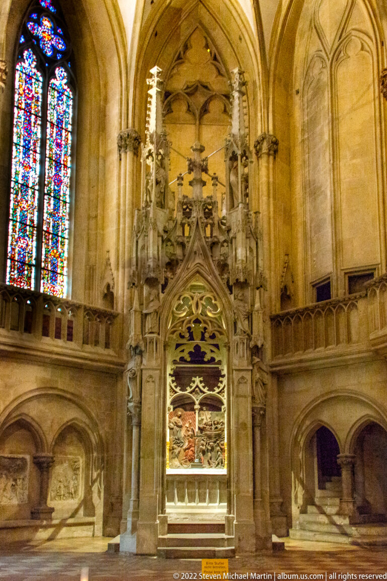Elaborate tall Gothic stone shrine with pointed canopy, carved figures, crucifix, and recessed painted panel.