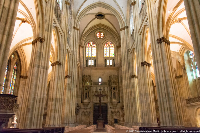 High Gothic cathedral interior with clustered stone piers, pointed arches, ribbed vaults, and stained-glass windows.