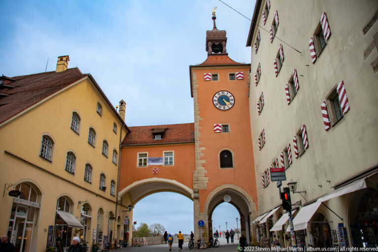 Orange Brückturm with clock, red-and-white shutters, and large arched gateway at the city end of Regensburg's Stone Bridge.