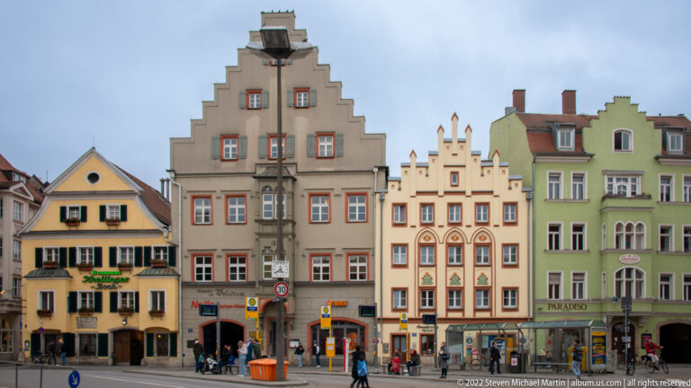 Colorful Regensburg townhouses with stepped gables, painted window trim, tall narrow façades, and shops at street level.