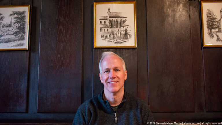 Seated man smiling in front of dark wood paneling and framed historical prints inside a Regensburg tavern.