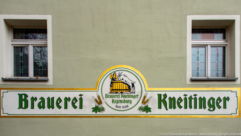 Painted Brauerei Kneitinger wall sign with green lettering, goat-and-barrel emblem, hop motifs, and Seit 1530 date.