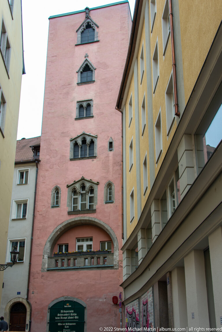 Pink historic building with stacked small windows, decorative surrounds, and a broad arched opening at street level.