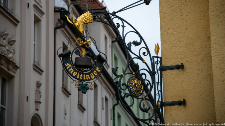 Decorative wrought-iron Kneitinger hanging sign with gilded accents projecting from a building façade.