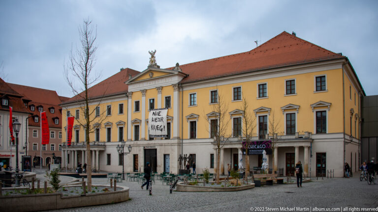 Yellow Theater Regensburg on Bismarckplatz with classical portico, red roof, and large NIE WIEDER KRIEG banner.
