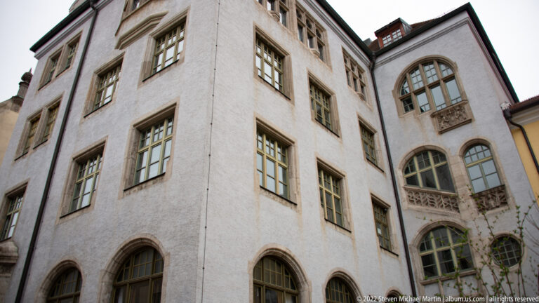 Upward view of pale historic building with arched lower windows, rectangular upper windows, and two decorative projecting balconies.