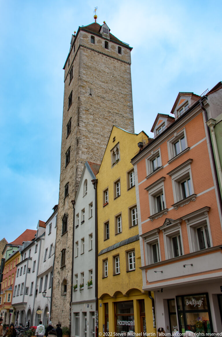 Tall medieval stone tower rising above colorful old-town houses in central Regensburg.