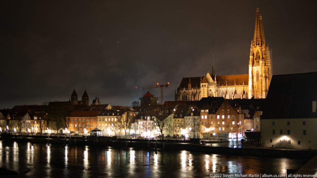 Night view across the Danube toward Regensburg's illuminated riverfront and St. Peter's Cathedral.