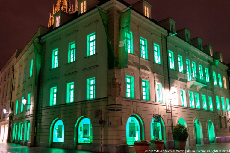 Large historic Regensburg building with arched ground floor and vivid green illumination across windows and façade.