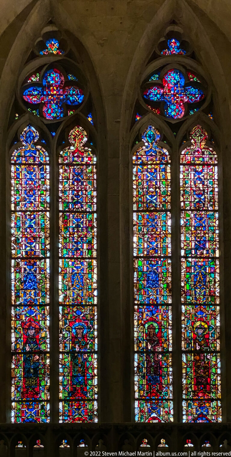 Four tall Gothic stained-glass lancets with vivid multicolored panels and circular tracery above.