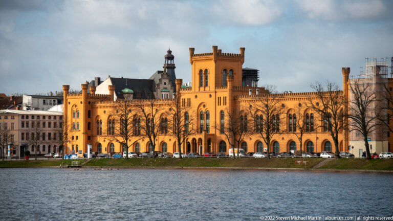 Long ochre historic building with arched windows and towers beside Pfaffenteich in Schwerin.