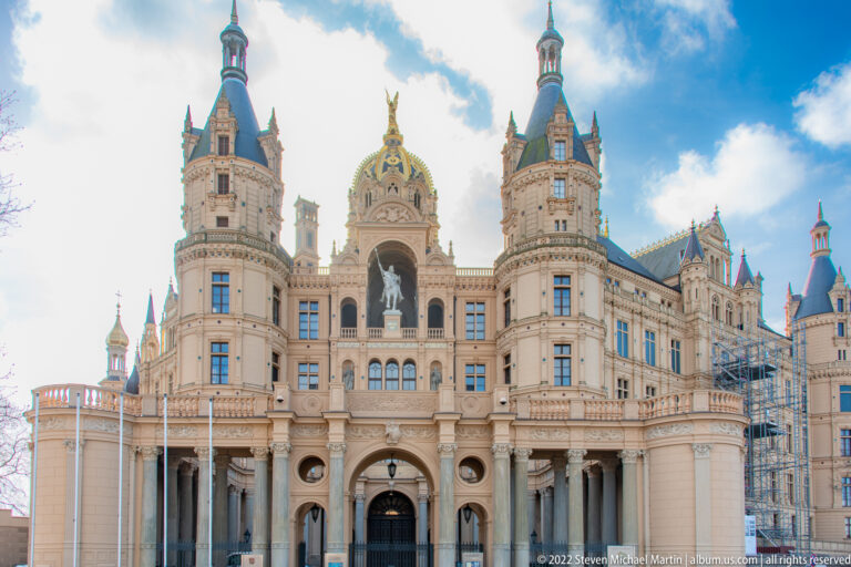 Ornate front façade of Schwerin Castle with towers, arched entrance, gilded dome, and scaffolding.