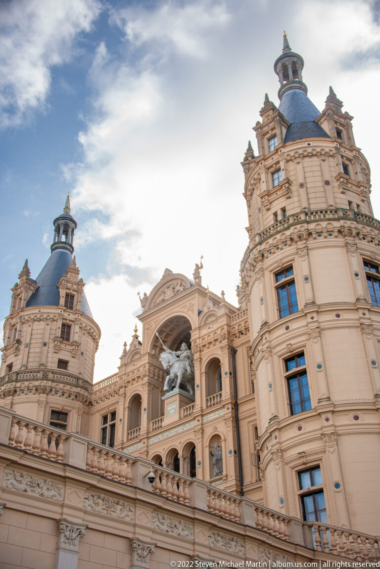 Low-angle view of ornate Schwerin Castle upper stories, rounded towers, and central equestrian figure.