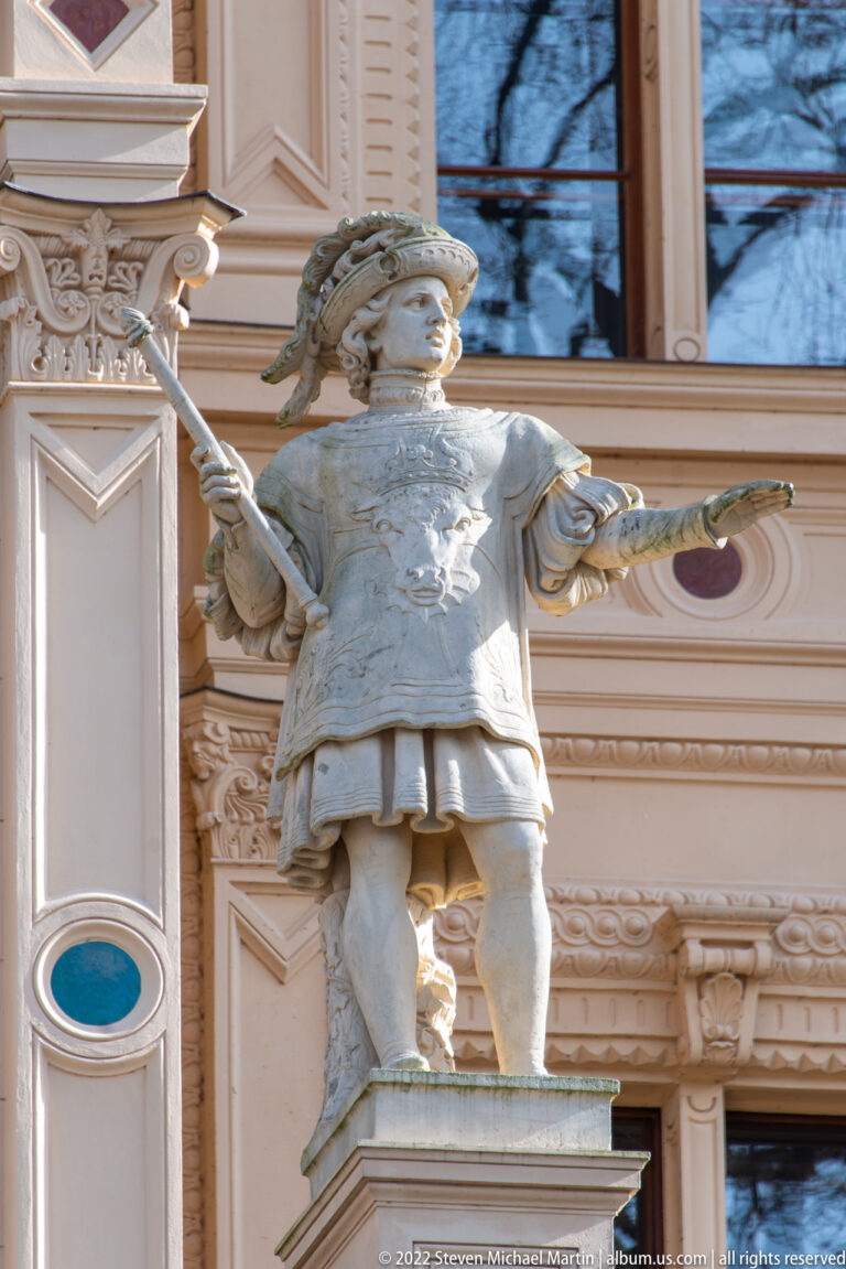 Stone male figure in historical costume holding a staff and shallow object on Schwerin Castle.