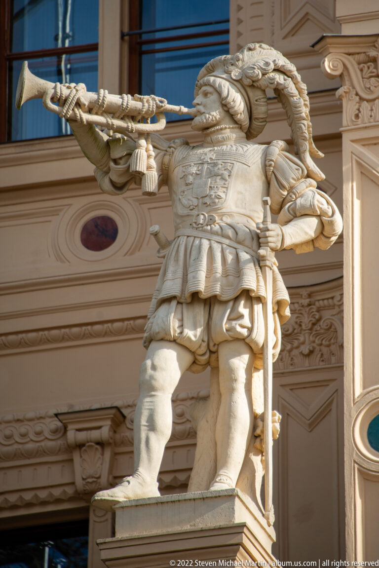 Carved trumpeter in feathered hat and tunic projecting from the façade of Schwerin Castle.
