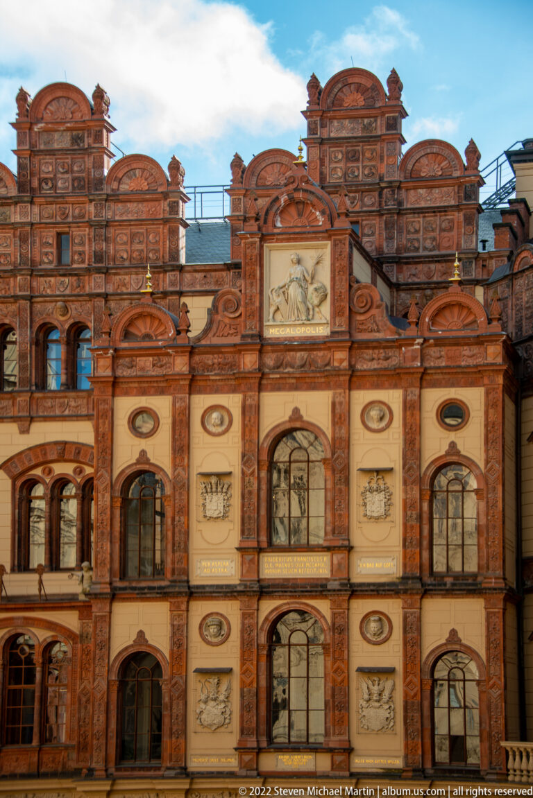 Ornate red-brick façade with arched windows, pale relief panels, and curved stepped gables.