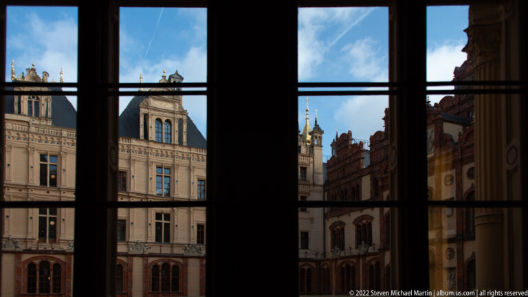 Schwerin Castle courtyard and towers seen through a dark multi-pane window.