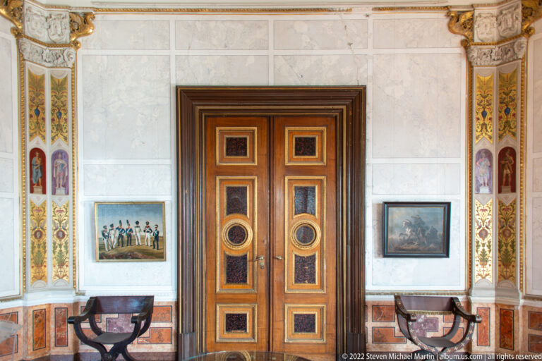 Paneled double doors centered between painted borders, framed scenes, and dark furniture in Schwerin Castle.
