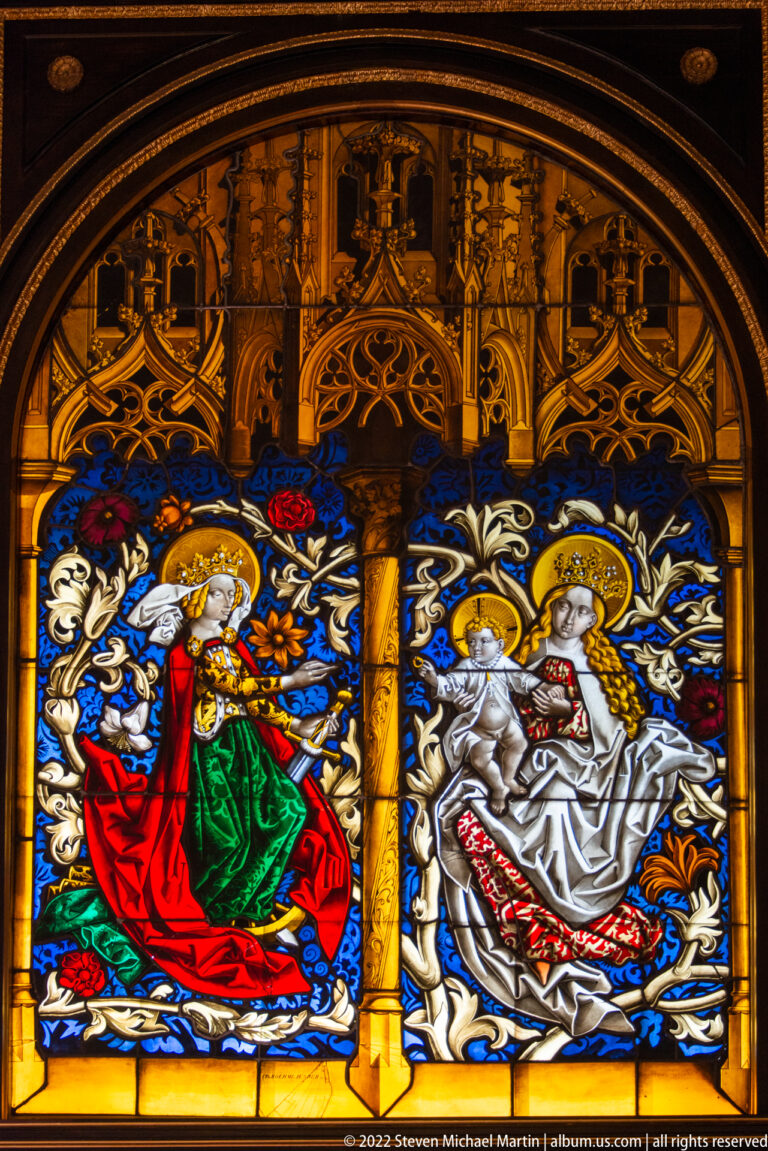 Colorful heraldic stained glass with two figure groups beneath Gothic tracery in Schwerin Castle.