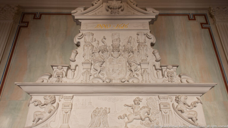 Ornate pale stone fireplace with heraldic crest, carved figures, scrollwork, and the inscription ANNO 1616.