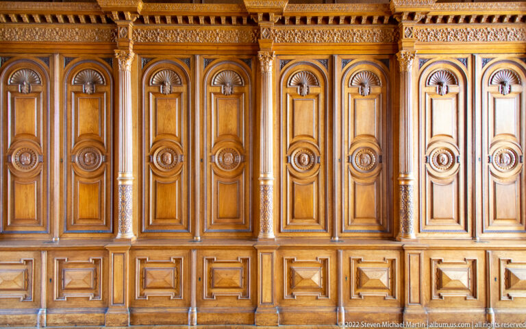 Close view of richly carved wooden wall panels with colonnettes, roundels, and geometric lower compartments.
