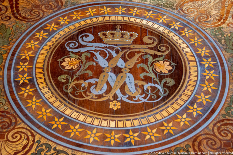 Round inlaid parquet medallion with crowned intertwined monogram, scrolling foliage, and geometric borders.