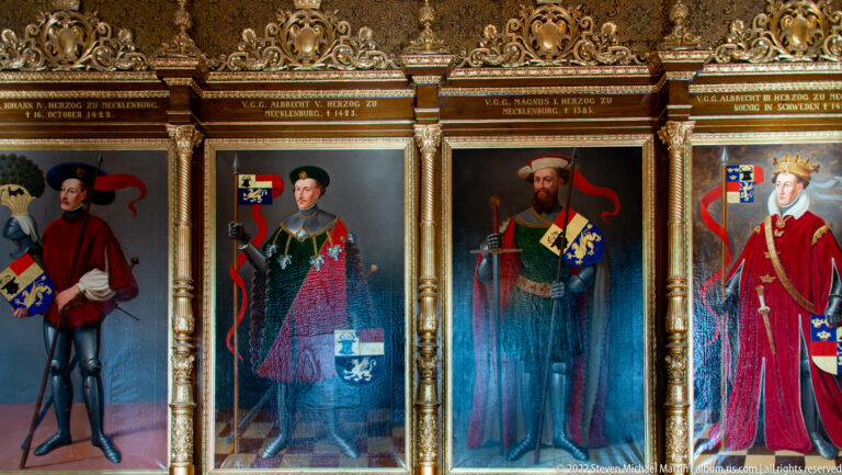 Four full-length dynastic portraits with inscriptions and coats of arms in gilded frames.