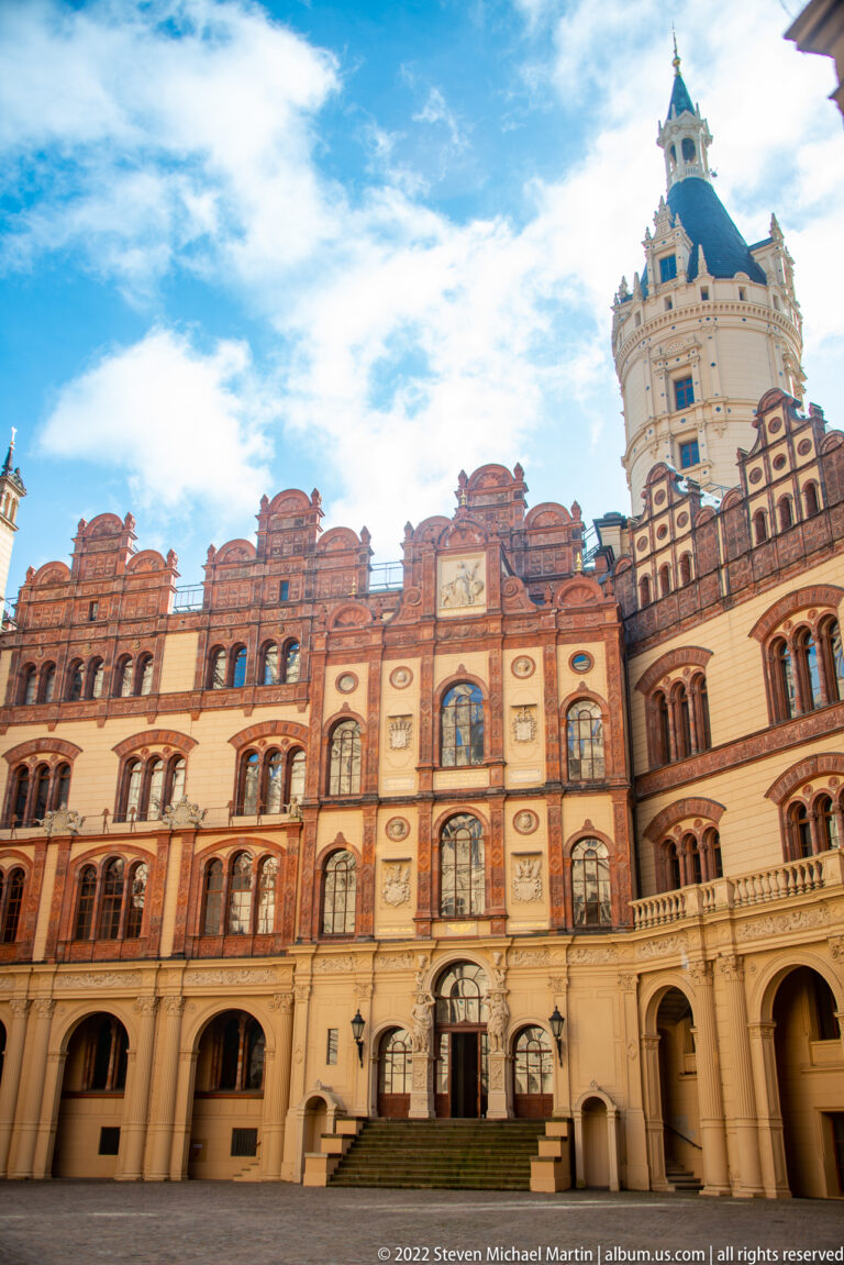 Schwerin Castle courtyard with pale arcades, red-brick gables, decorated façades, and tall tower.
