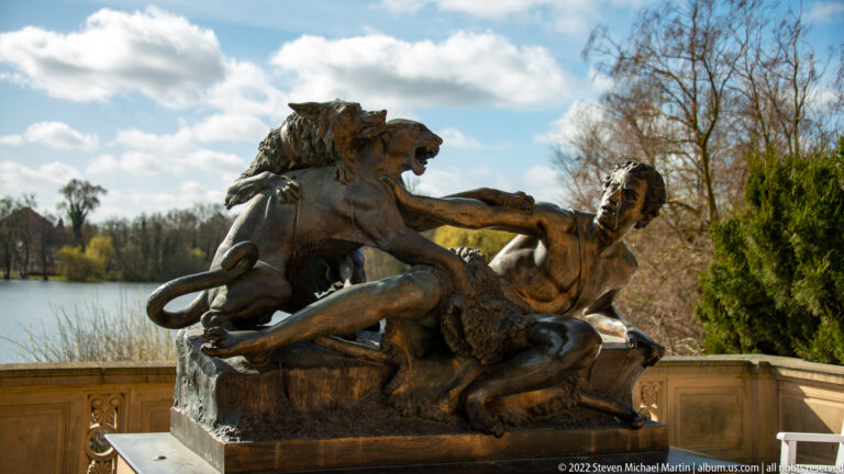 Bronze garden group of a shepherd and dog struggling with an attacking panther beside the lake.