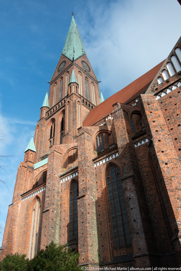 Oblique low-angle view along Schwerin Cathedral’s brick side wall, windows, buttresses, and tower.