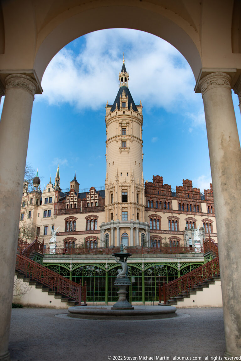 Schwerin Castle tower and courtyard framed by an Orangerie arch and pale columns.