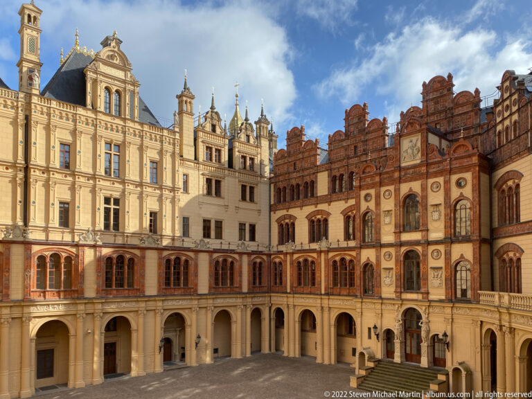 Wide Schwerin Castle courtyard with pale arcades, towered wings, red-brick stepped gables, and decorated façades.