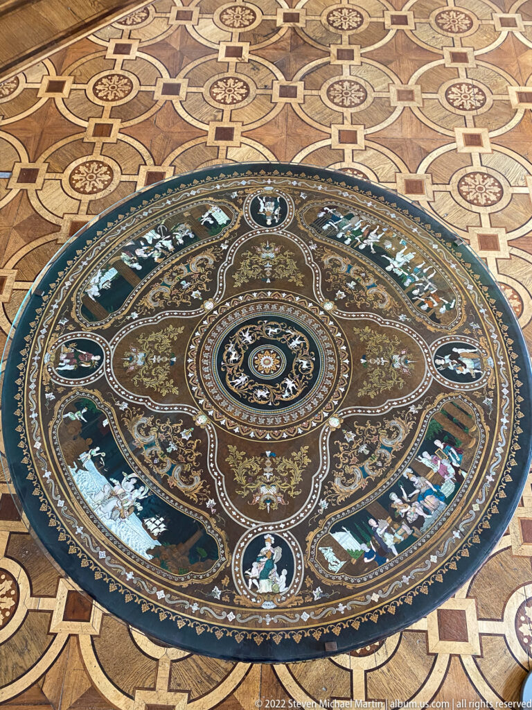 Large circular inlaid floor medallion with floral scrolls, small figures, birds, and concentric ornament set into geometric parquet.