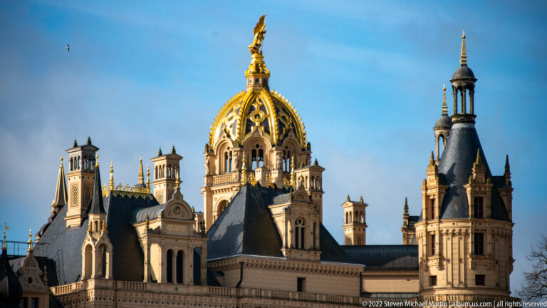 Gilded openwork dome and ornate towers rising above the slate roofs of Schwerin Castle.
