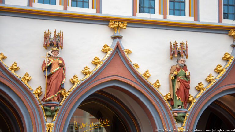 Two painted standing figures above pointed arches, surrounded by gilded finials and decorative Gothic tracery.