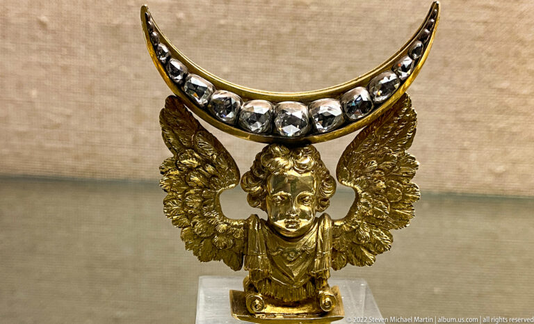 Gilded winged bust supporting a crescent-shaped ornament set with a row of clear faceted stones.