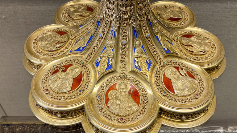 Gold ecclesiastical object with multiple round medallions of sacred figures, red grounds, blue enamel, and filigree.