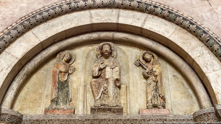 Semicircular stone tympanum with seated Christ and two standing haloed figures beneath carved ornamental archivolts.
