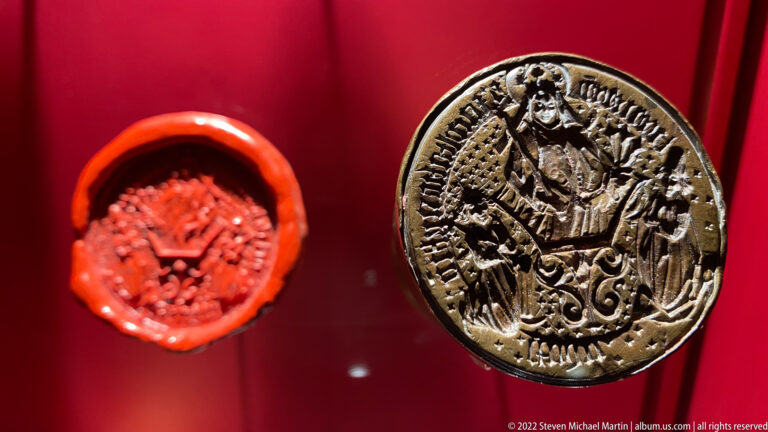 Red wax seal impression beside a circular metal seal matrix engraved with an enthroned clerical figure and inscription.