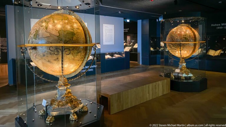 Two large historic globes in glass cases with painted surfaces, broad rings, and ornate gilded bases.