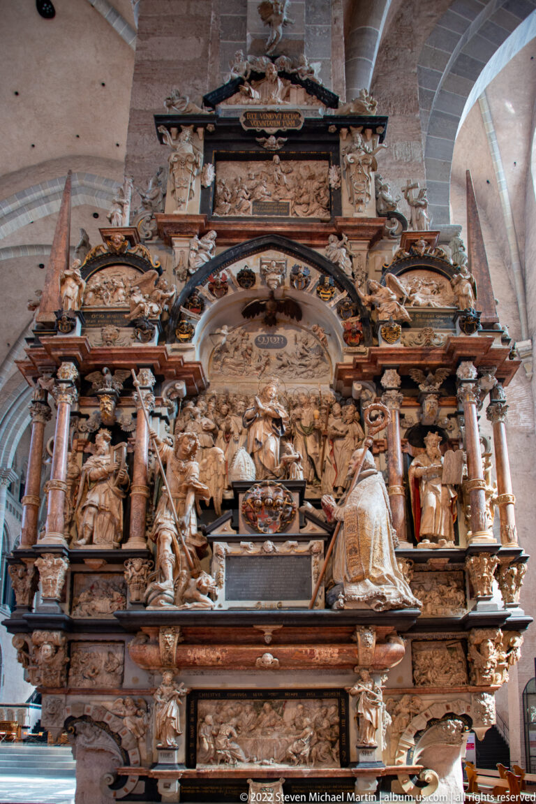 Large warm-toned carved altarpiece with multiple tiers of figures, relief scenes, columns, and architectural ornament.