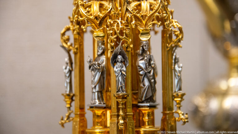 Silver-toned saint figures standing beneath gilded Gothic-style canopies on a richly ornamented liturgical object.