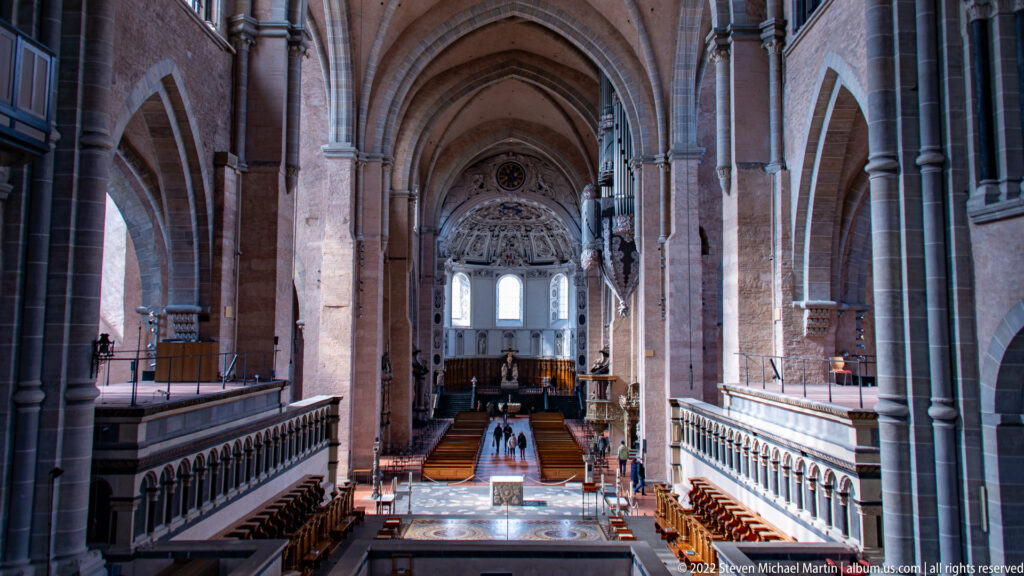 Elevated view down Trier Cathedral nave toward the choir, with massive piers, arches, galleries, and seating.