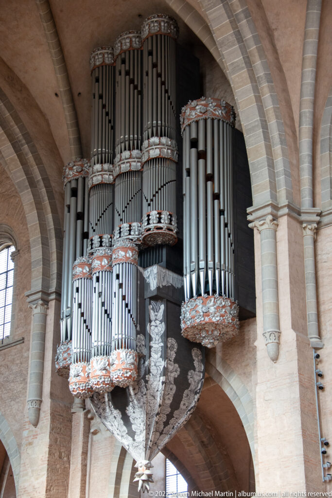Large cathedral pipe organ with grouped metal pipes and carved cases mounted beneath pale stone vaults.