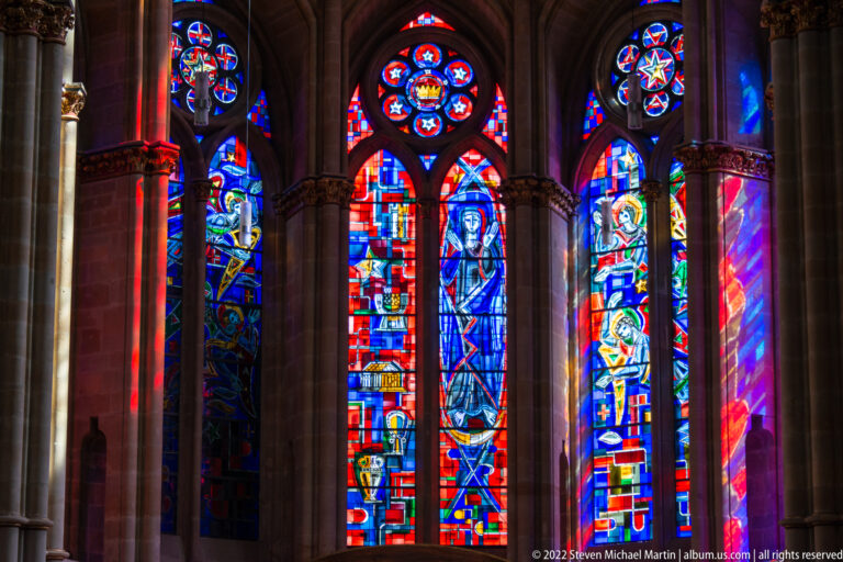Several vivid stained-glass windows in pointed Gothic bays, with colored light falling across stone columns and arches.