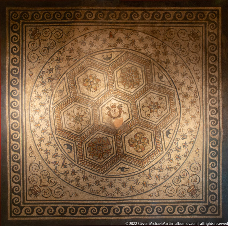 Octagonal Roman mosaic with a central figurative panel, surrounding floral medallions, vine scrolls, and geometric borders.