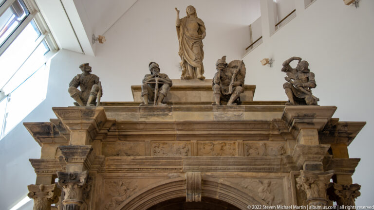 Carved Roman stone monument with an arched opening and multiple standing and seated figures along the upper ledge.