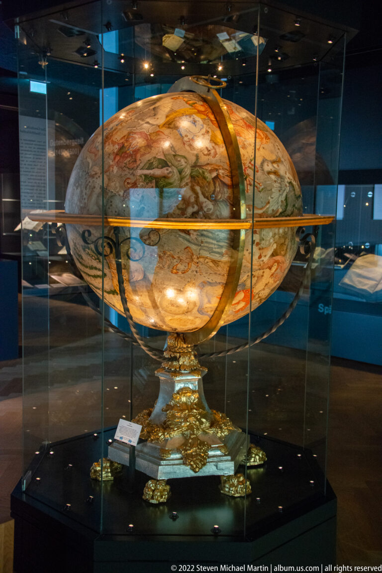 Large painted terrestrial globe on an ornate gilded stand inside a glass museum case.