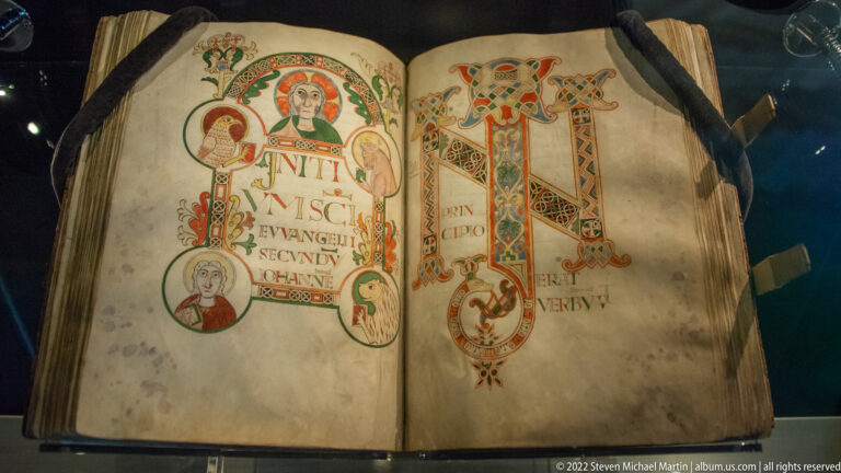 Open illuminated manuscript with two large interlaced initials in red, green, blue, and gold and small portrait medallions.